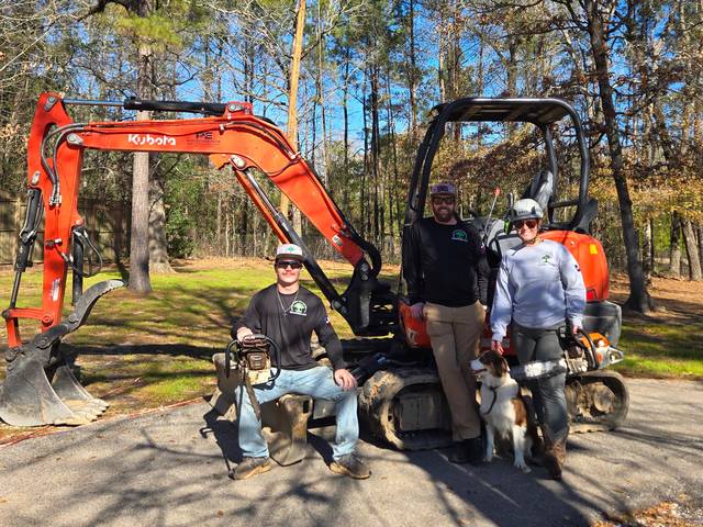 Three Branching Out crew members and two dogs in front of a pair of tracked excavators