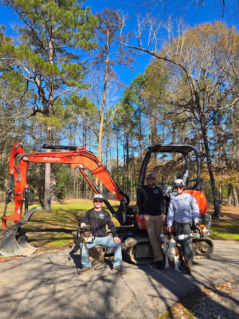 Three Branching Out crew members and two dogs in front of a pair of tracked excavators