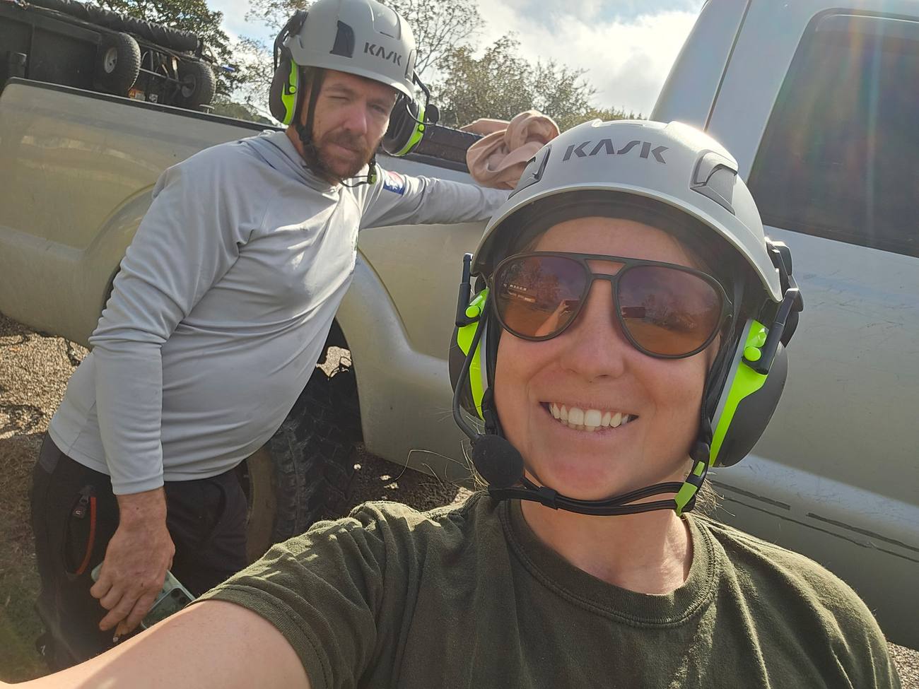 Two crew members in climbing helmets with ear and eye protection, beside a work truck