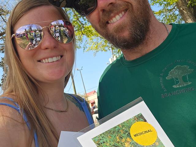 Two people holding a printed native plant identification sheet for Saint John's Wort