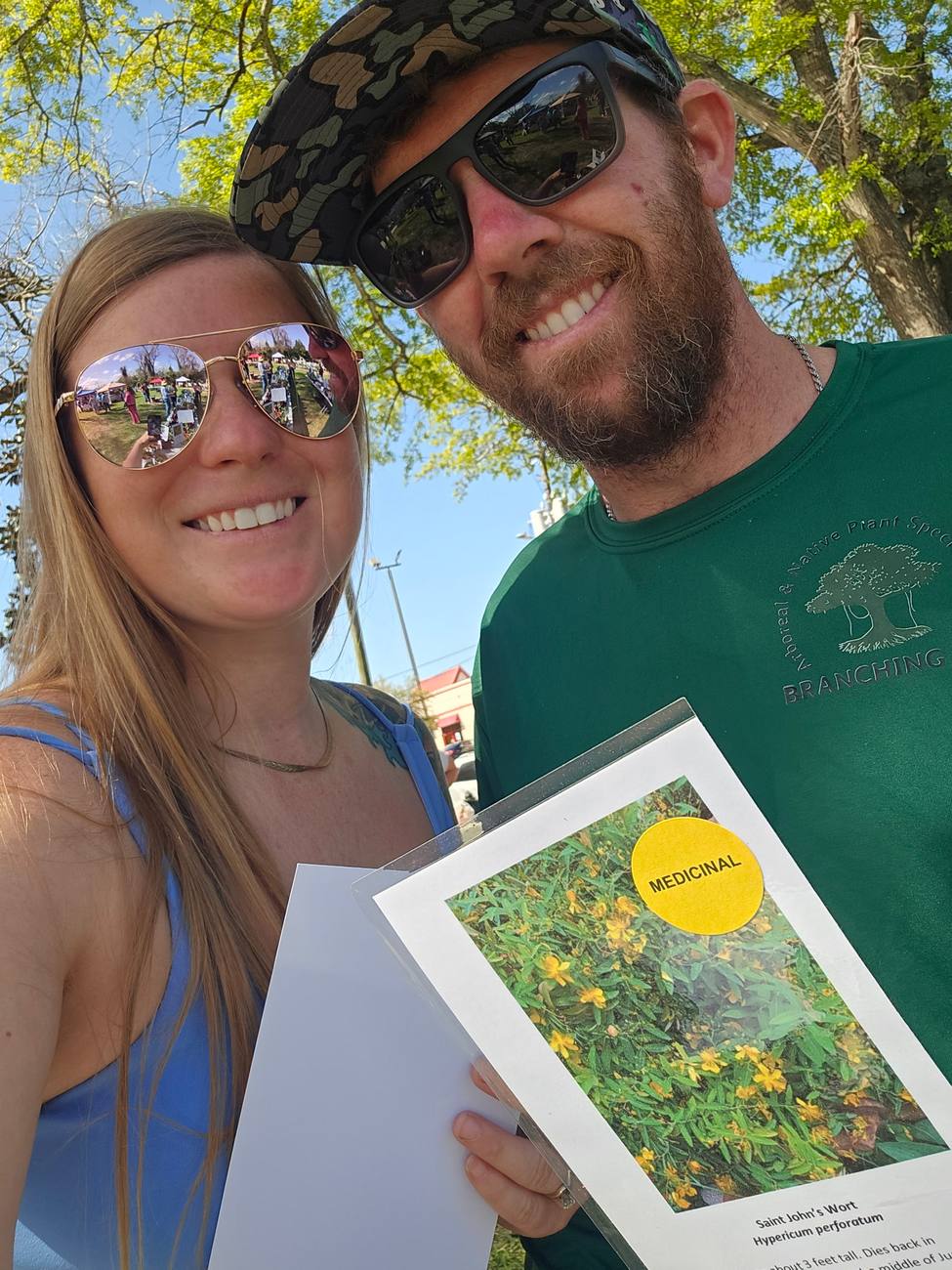 Two people holding a printed native plant identification sheet for Saint John's Wort