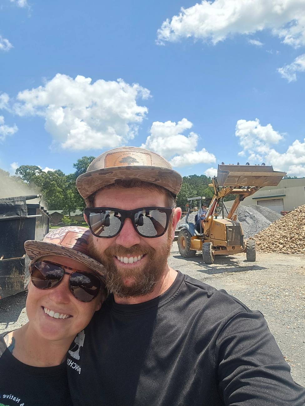 Two crew members at a materials yard, with a loader working piles of crushed rock and gravel